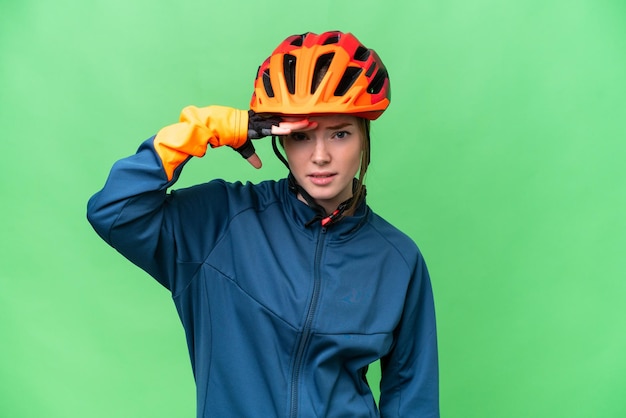 Junge Radfahrerin über isoliertem Chroma-Key-Hintergrund, die mit der Hand weit wegschaut, um etwas zu sehen