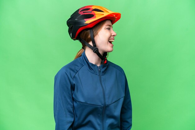 Junge Radfahrerin über isoliertem Chroma-Key-Hintergrund lachend in Seitenlage