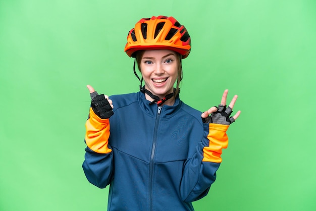 Junge Radfahrerin über isoliertem Chroma-Key-Hintergrund mit OK-Zeichen und Daumen-nach-oben-Geste
