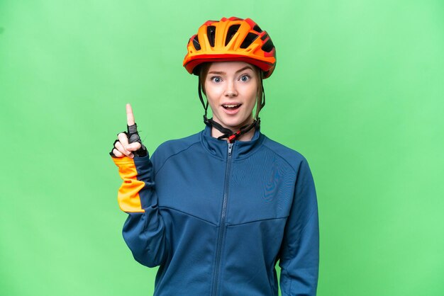 Junge Radfahrerin vor isoliertem Chroma-Key-Hintergrund denkt an eine Idee und zeigt mit dem Finger nach oben