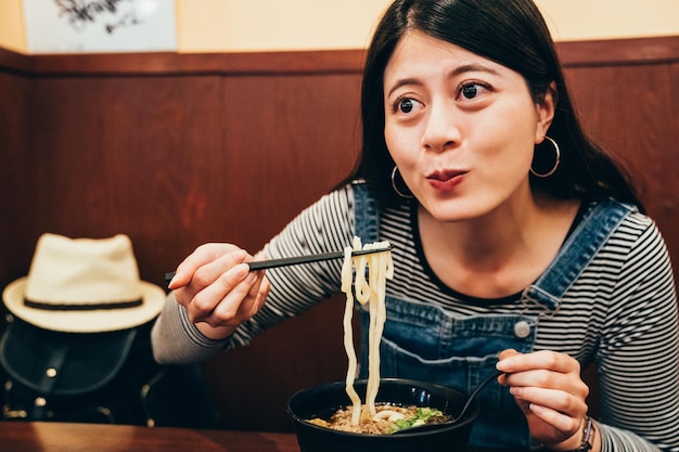 junge Reisende, die hungrig Udon-Nudeln im Izakaya essen. chinesin beim abendessen mit leckerer japanischer küche in reisereise osaka japan. Joufully Dame, die die Mahlzeit kaut, die drinnen sitzt.