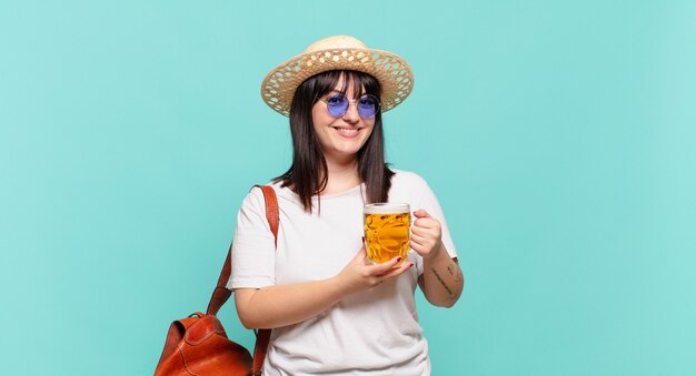 Junge reisende Frau, die glücklich mit einer Hand auf der Hüfte und selbstbewusster, positiver, stolzer und freundlicher Haltung lächelt