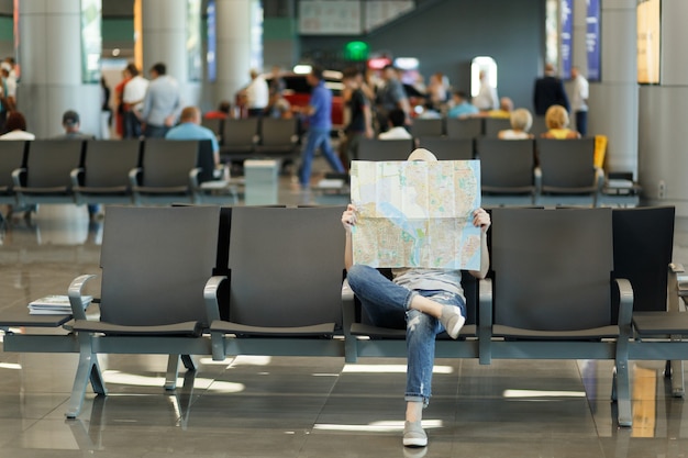 Junge reisende Touristenfrau, die mit Papierkarte bedeckt, Route sucht, in der Lobbyhalle am internationalen Flughafen wartet?