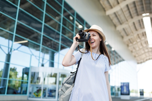 Junge reisende Touristenfrau mit Rucksack, die Fotos auf Retro-Vintage-Fotokamera am internationalen Flughafen macht