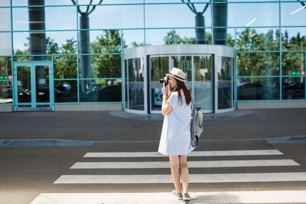 Junge reisende Touristenfrau mit Rucksack fotografieren auf Retro-Vintage-Fotokamera auf Zebrastreifen am internationalen Flughafen international