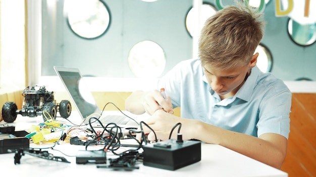 Junge repariert das Hauptbrett, während er Bau mit Hilfe eines Laptops studiert