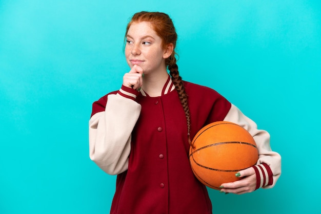 Junge rötliche Frau spielt Basketball isoliert auf blauem Hintergrund und blickt nach oben