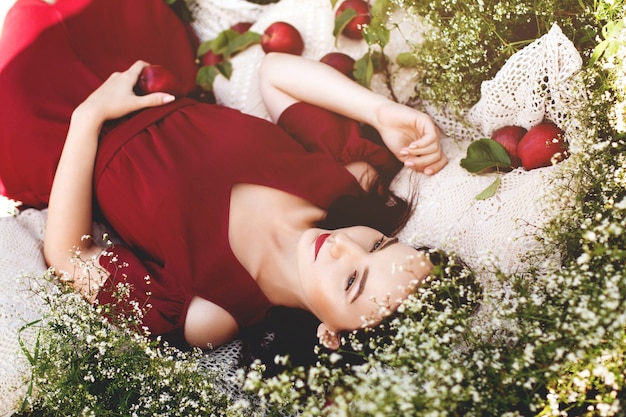 Junge romantische Frau im roten Kleid, das im sonnigen Sommertag des Grases liegt