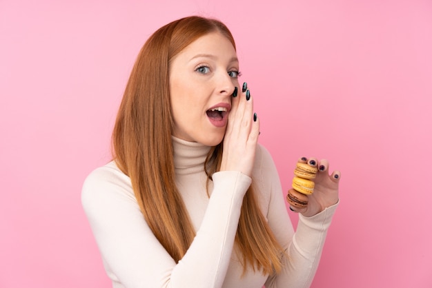 Junge rothaarige Frau, die bunte französische Macarons hält und etwas flüstert