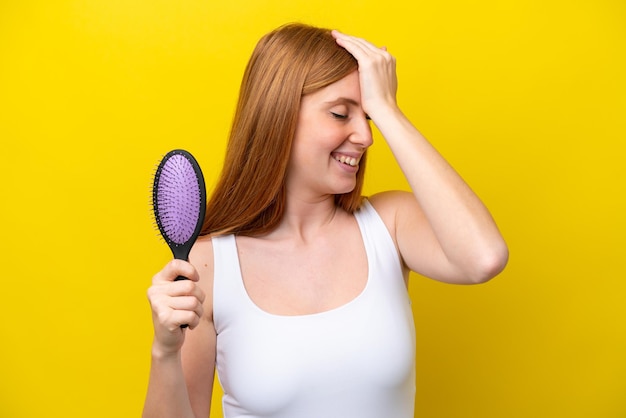 Junge rothaarige Frau, die eine auf weißem Hintergrund isolierte Haarbürste hält, hat etwas erkannt und beabsichtigt die Lösung