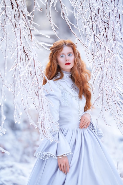 Junge rothaarige Frau, eine Prinzessin, geht in einem blauen Kleid in einem Winterwald spazieren