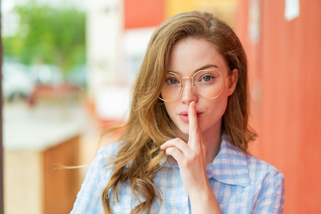 Junge rothaarige Frau im Freien mit Brille und Schweigegeste