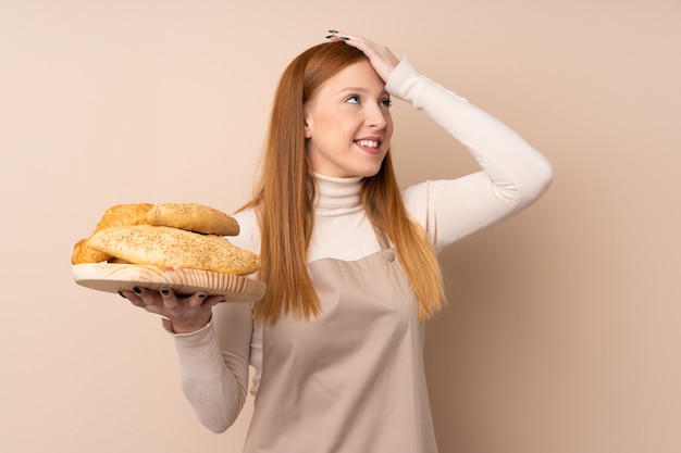 Junge rothaarige Frau in der Kochuniform. Bäckerin, die einen Tisch mit mehreren Broten hält