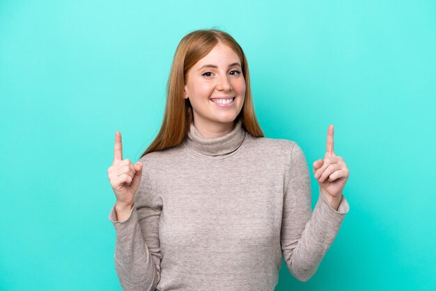 Junge rothaarige Frau isoliert auf blauem Hintergrund, die auf eine großartige Idee zeigt