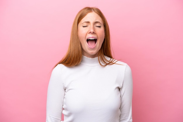 Junge rothaarige Frau isoliert auf rosa Hintergrund, die mit weit geöffnetem Mund nach vorne schreit
