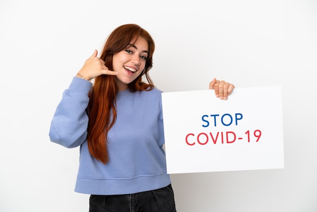 Junge rothaarige Frau isoliert auf weißem Hintergrund, die ein Plakat mit dem Text Stop Covid 19 hält und Telefongeste macht