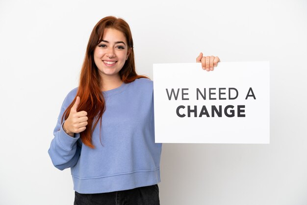 Foto junge rothaarige frau isoliert auf weißem hintergrund, die ein plakat mit dem text we need a change mit daumen nach oben hält