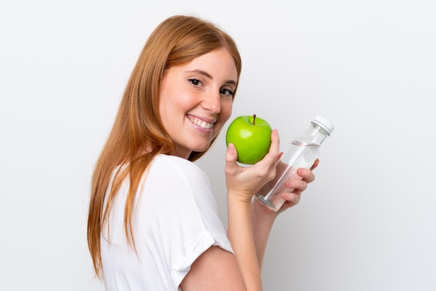 Junge rothaarige Frau isoliert auf weißem Hintergrund mit einem Apfel und mit einer Flasche Wasser