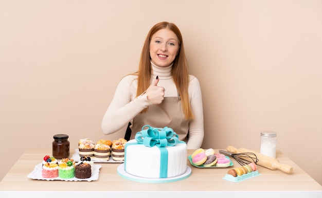 Junge rothaarige Frau mit einem großen Kuchen, der eine Daumen hoch Geste gibt