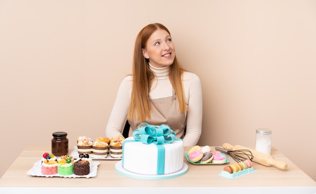 Junge rothaarige Frau mit einem großen Kuchen, der lacht und aufschaut