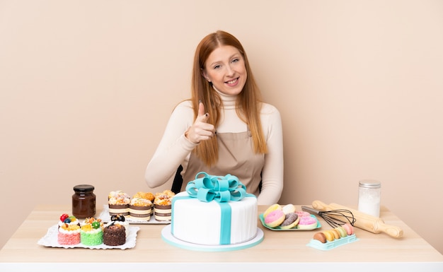 Junge rothaarige Frau mit einem großen Kuchen zeigt Finger auf Sie