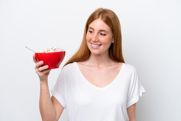 Junge rothaarige Frau mit einer Schüssel Müsli isoliert auf weißem Hintergrund mit glücklichem Ausdruck