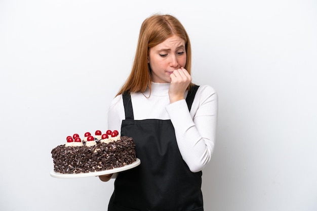 Junge rothaarige Frau mit Geburtstagstorte isoliert auf weißem Hintergrund mit Zweifeln