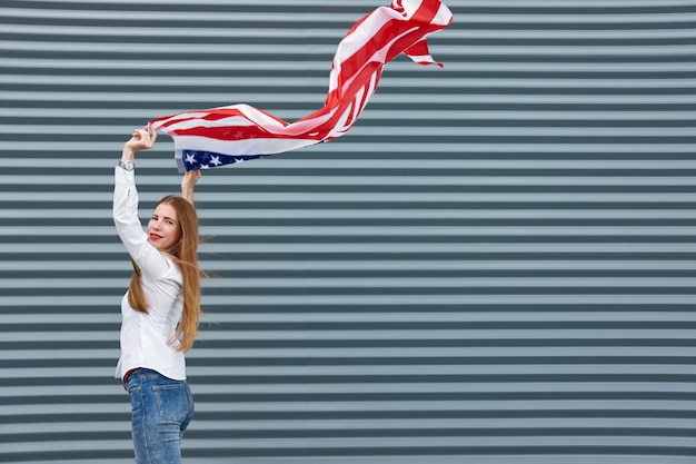 Junge rothaarige Frau mit rot gestrichenen Lippen, die mit der USA-Flagge stehen