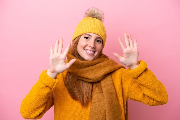 Junge rothaarige Frau mit Winterjacke isoliert auf rosa Hintergrund, die zehn mit den Fingern zählt