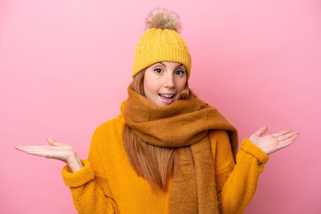 Junge rothaarige Frau mit Winterjacke isoliert auf rosa Hintergrund mit schockiertem Gesichtsausdruck