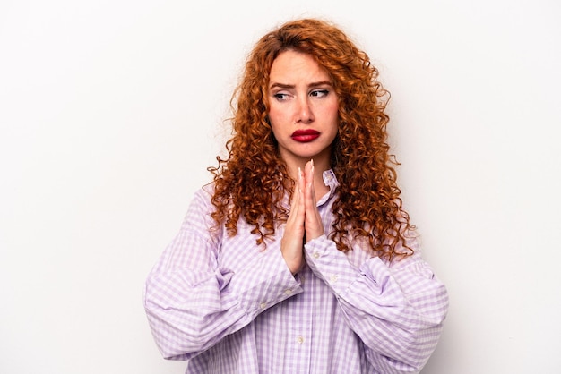 Junge rothaarige kaukasische Frau isoliert auf weißem Hintergrund betend und Hingabe zeigende religiöse Person auf der Suche nach göttlicher Inspiration
