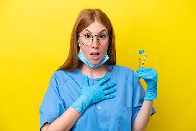 Junge rothaarige Zahnarztfrau isoliert auf gelbem Hintergrund überrascht und schockiert, während sie nach rechts schaut