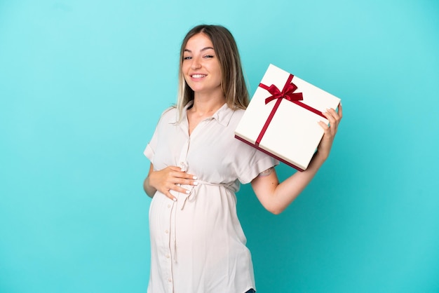 Junge rumänische Frau isoliert auf blauem Hintergrund schwanger und hält ein Geschenk