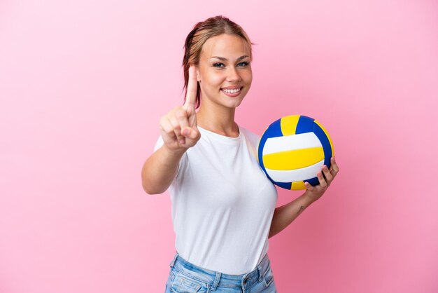 Junge Russin, die Volleyball spielt, isoliert auf rosa Hintergrund, zeigt und hebt einen Finger