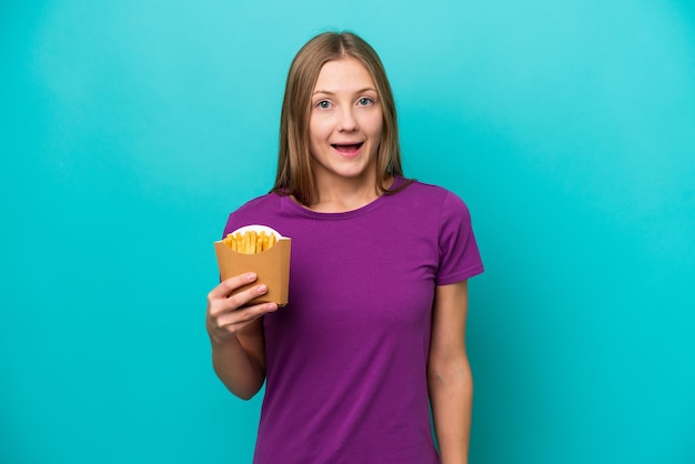 Junge Russin fängt Pommes frites isoliert auf blauem Hintergrund mit überraschendem Gesichtsausdruck