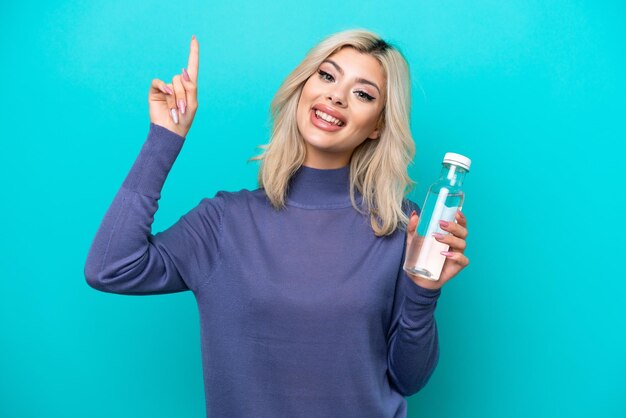 Junge Russin mit einer Flasche Wasser isoliert auf blauem Hintergrund, die einen Finger im Zeichen der Besten zeigt und hebt