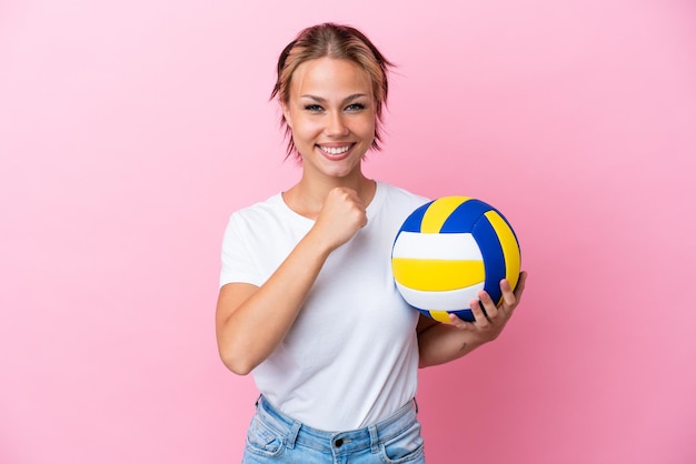 Junge Russin spielt Volleyball isoliert auf rosa Hintergrund und feiert einen Sieg
