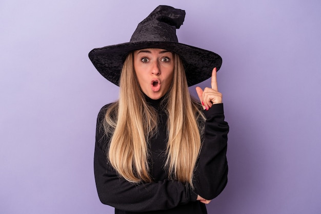 Junge Russin verkleidet als Hexe, die Halloween feiert, isoliert auf violettem Hintergrund mit einer großartigen Idee, Konzept der Kreativität.