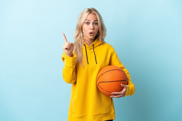 Junge russische Frau, die Basketball spielt, isoliert auf Blau, das beabsichtigt, die Lösung zu verwirklichen, während ein Finger anhebt