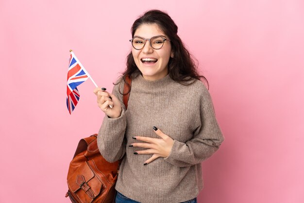 Junge russische Frau, die eine britische Flagge lokalisiert auf rosa Hintergrund hält, der viel lächelt