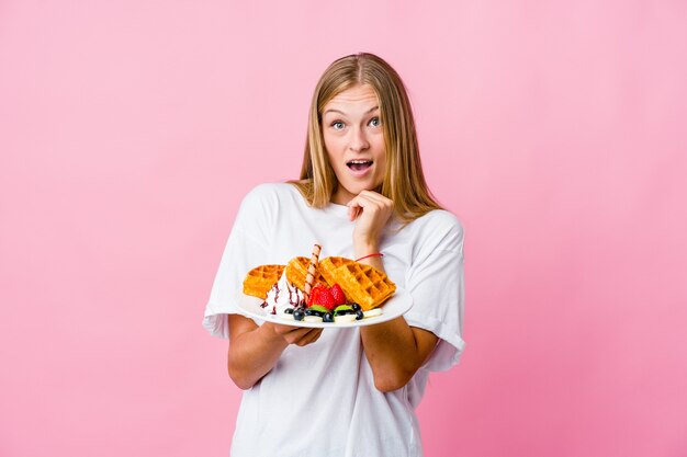 Junge russische Frau, die eine Waffel isst, die für Glück betet, erstaunt und Mund öffnet, der nach vorne schaut.