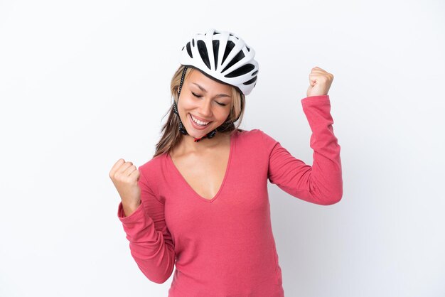 Junge russische Frau, die einen Fahrradhelm trägt, isoliert auf weißem Hintergrund, der einen Sieg feiert