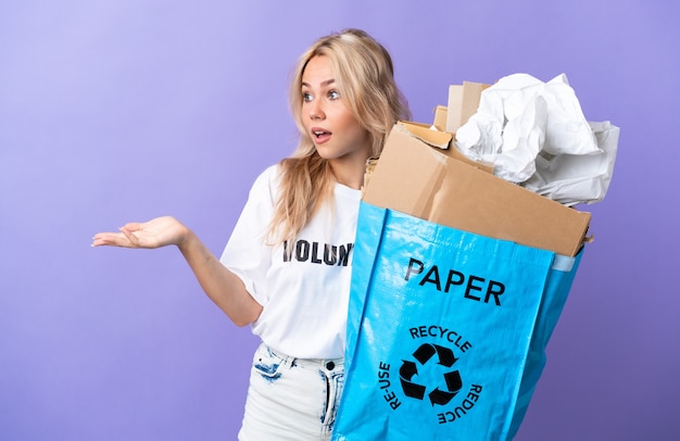 Junge russische Frau, die einen Recyclingbeutel voll des Papiers hält, um lokalisiert auf Purpur mit Überraschungsausdruck beim Betrachten der Seite zu recyceln