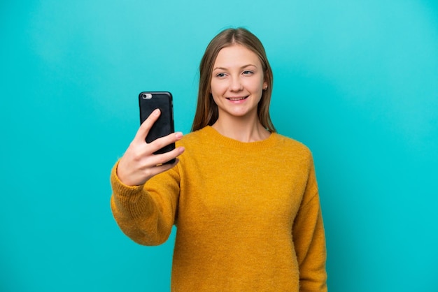 Junge russische Frau isoliert auf blauem Hintergrund, die ein Selfie mit dem Handy macht