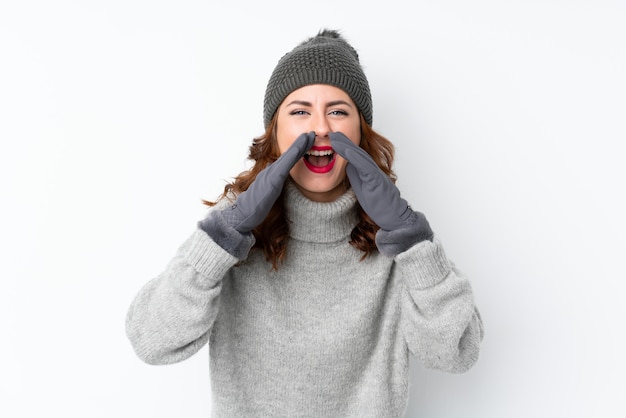 Foto junge russische frau mit winterhut über dem lokalisierten weiß, das mit dem breiten mund schreit, öffnen sich