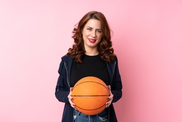 Junge russische Frau über getrenntem Rosa mit Kugel des Basketballs