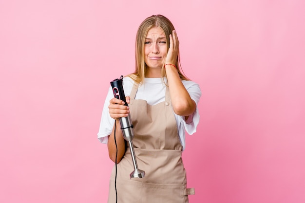 Junge russische Kochfrau, die einen elektrischen Mixer hält, der trostlos jammert und weint.