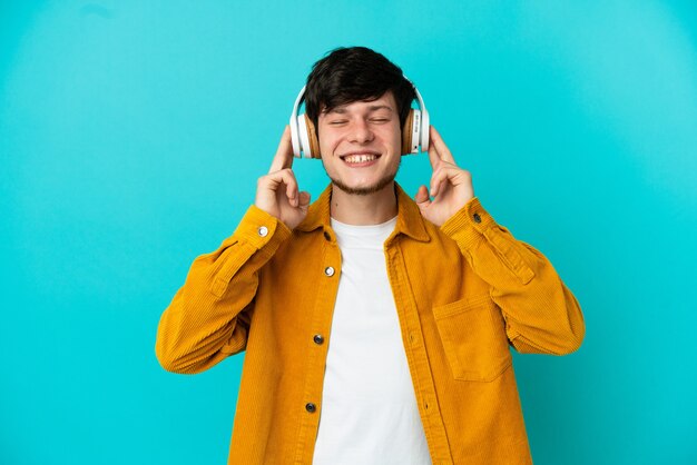 Junge russische Mann isoliert auf blauem Hintergrund Musik hören
