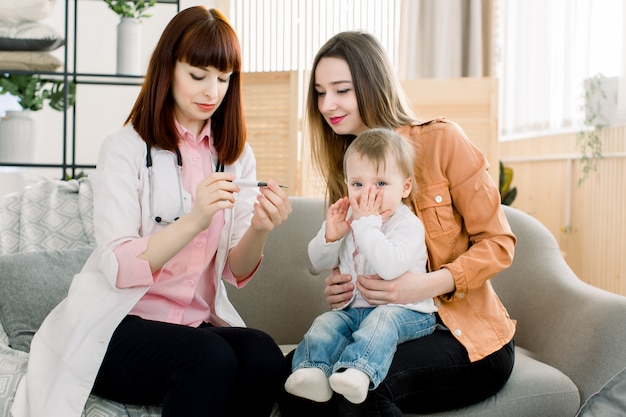 Junge Ärztin, die die Temperatur des Babykindes misst. Arzt nimmt die Temperatur des Babys