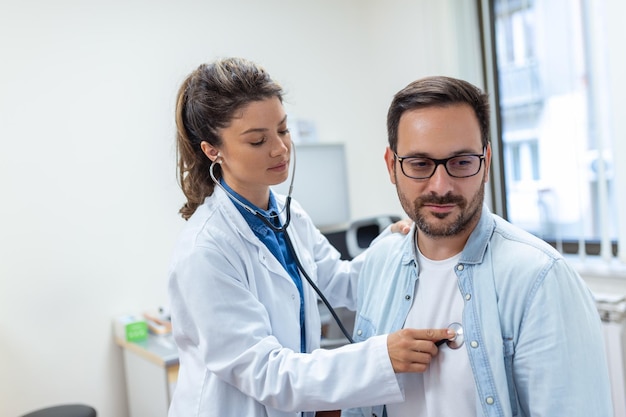 Junge Ärztin hört bei einem Kliniktreffen auf die Herzbrust des männlichen Patienten mit Stethoskop